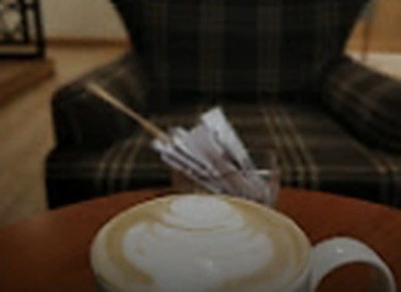 Cappuccino coffee latte on a wooden table beside a tartan armchair