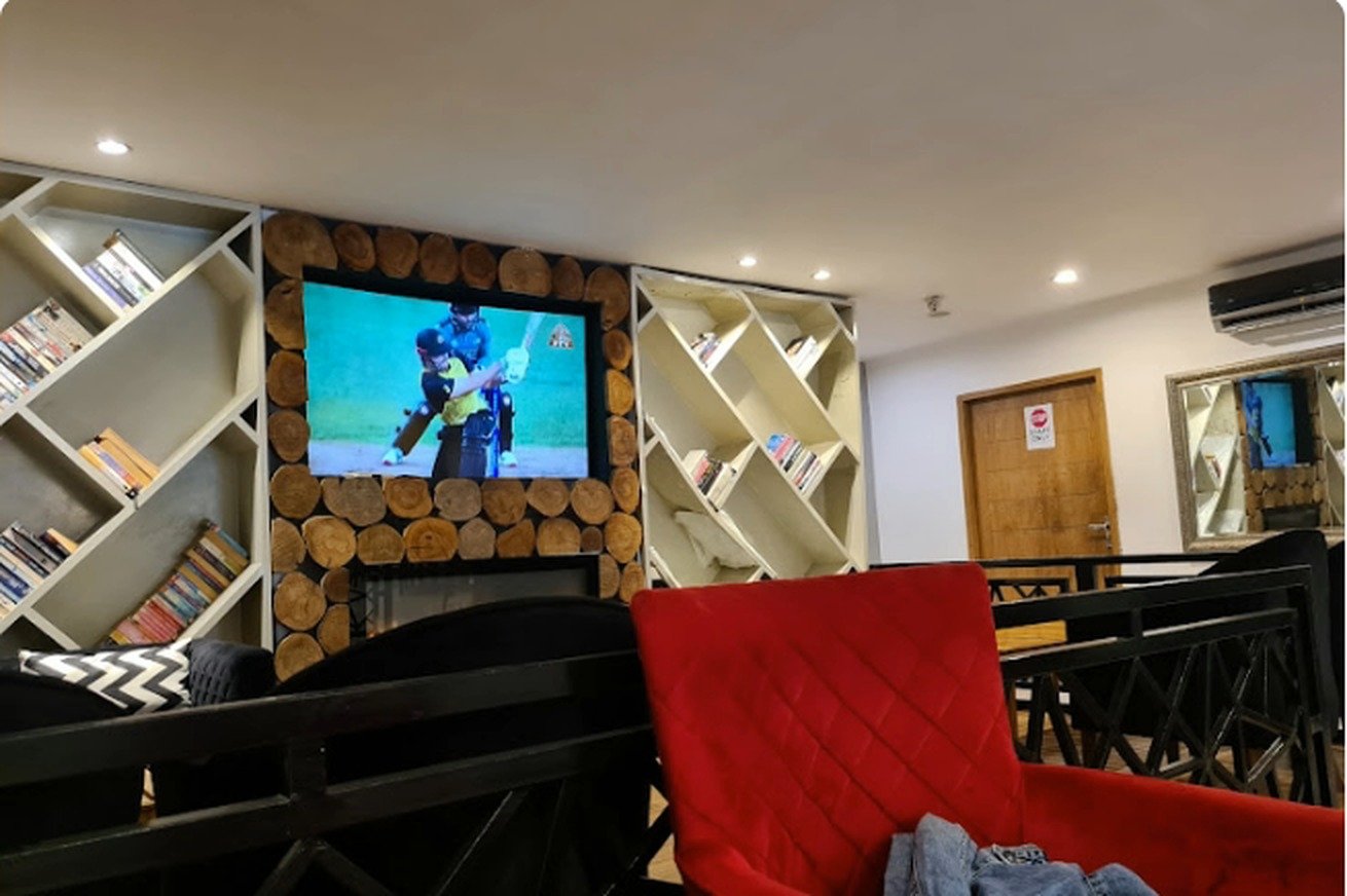 Book-lined lounge with log-wall TV and red sofa inside Second Cup Johar Town